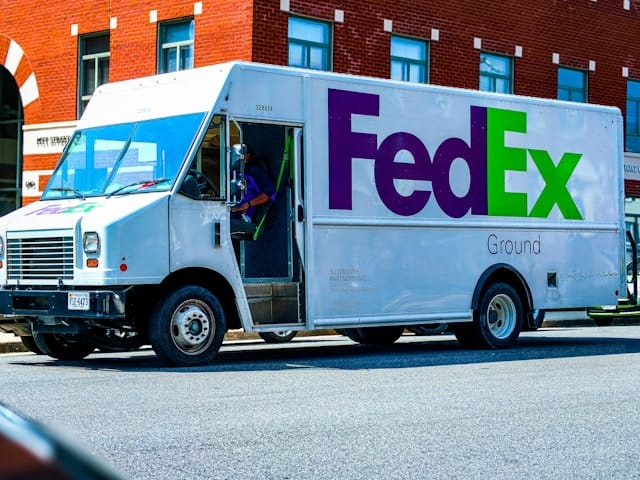 A FedEx truck in front of a brick building. An arrow is left in the whitespace between the E and the x